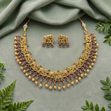 Gold-toned traditional necklace and matching earrings with elephant motifs, pink gemstone teardrops, and small green stone accents, arranged on a soft sage-green fabric backdrop with decorative leaves around the edges.