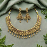 An ornate gold-toned traditional necklace and matching earrings set with small multicolored gemstone accents, arranged on a soft sage green fabric backdrop with decorative green leaves around the edges.