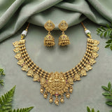 Gold-toned traditional Indian jewelry set featuring a statement necklace and matching dangle earrings, styled on a sage green draped fabric background with decorative green leaves.