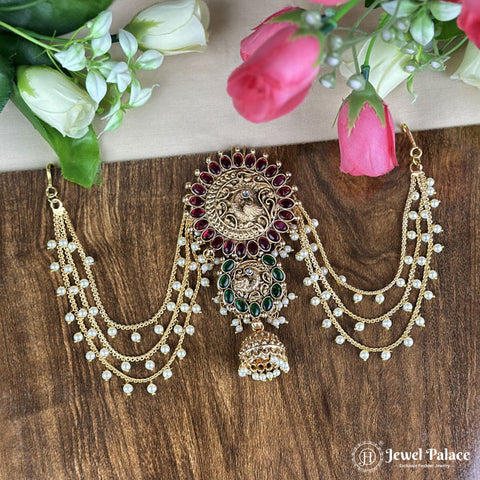 Ornate gold necklace with red and green stones on a wooden surface with flowers.