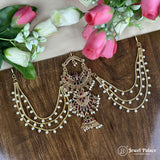 Ornate gold necklace with gemstones on a wooden surface with flowers