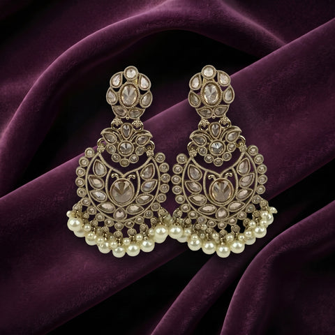 A pair of ornate gold-toned chandelier earrings with clear stones and white pearl fringe, displayed on draped deep purple velvet fabric.
