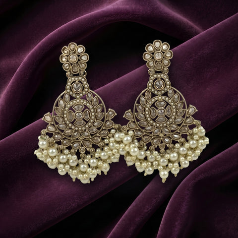 A pair of ornate gold-toned chandelier earrings with intricate stone work and dangling pearl clusters, displayed on draped deep purple velvet fabric.