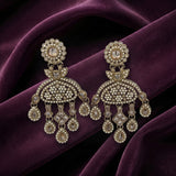 A pair of ornate gold-toned chandelier earrings embellished with clear stones and small pearl-like beads, displayed on draped deep purple fabric.