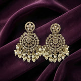 A pair of ornate gold-toned chandelier earrings with intricate filigree work, clear stones, and dangling pearl-like beads, displayed on draped deep purple velvet fabric.