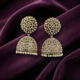 A pair of ornate Indian jhumka earrings with intricate gold-toned filigree and clear stones, displayed on draped deep purple velvet fabric.