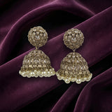 A pair of ornate Indian jhumka earrings with intricate silver-toned filigree work, clear stones, and dangling pearl-like beads, displayed on draped deep purple velvet fabric.