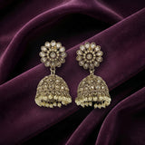 A pair of ornate Indian jhumka earrings with gold-toned filigree, clear stone embellishments, and dangling pearl-like beads, displayed on draped deep purple velvet fabric.