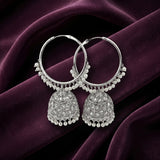 A pair of silver-toned Indian jhumka hoop earrings with intricate filigree detailing and dangling pearl bead borders, displayed on draped dark purple velvet fabric.