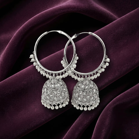 A pair of silver-toned Indian jhumka hoop earrings with intricate filigree detailing and dangling pearl bead borders, displayed on draped dark purple velvet fabric.