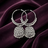 A pair of silver-toned Indian jhumka earrings with intricate beadwork and dangling pearl-like beads, displayed on draped deep purple velvet fabric.