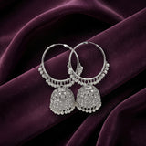 A pair of silver-toned Indian jhumka earrings with intricate filigree work and bead borders, displayed on draped deep purple velvet fabric.