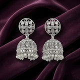 A pair of silver-toned Indian jhumka earrings with clear stones and white pearls, displayed on a draped dark purple velvet fabric background.