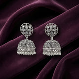 A pair of silver-toned Indian jhumka earrings with intricate filigree work and pearl bead fringe, displayed on draped deep purple velvet fabric.
