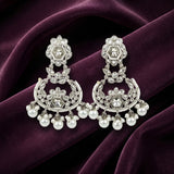A pair of silver-toned chandelier earrings adorned with clear crystals and white pearls, displayed on a draped deep purple velvet fabric.