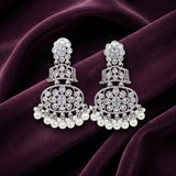 A pair of silver-toned traditional Indian chandelier earrings adorned with clear stones and white pearl drops, displayed on a draped dark purple velvet fabric.