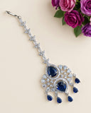 A silver-toned choker headband decorated with clear crystals and deep blue gemstones, displayed on a light beige background with purple roses in the corner.