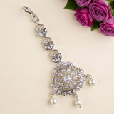 A silver-toned ornate jewelry clasp or keychain charm decorated with clear rhinestones and white pearl drops, displayed on a light beige background with pink roses in the top right corner.