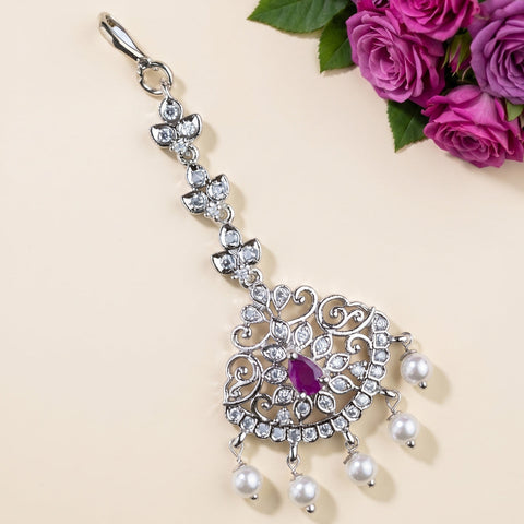 A silver-toned traditional Indian choker necklace with a central purple gemstone and dangling white pearls, styled on a beige background with pink roses in the corner.