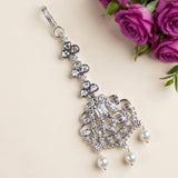 A silver-toned choker necklace with clear rhinestones and white faux pearls, styled on a light beige background with purple roses in the corner.