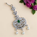 A silver-toned traditional Indian jhumka earring decorated with clear crystals, a central green stone, and three dangling white pearls, displayed on a beige background with pink roses in the corner.