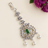 A silver-toned ornate dangle earring with a central green stone and white pearl drops, displayed on a light beige background with purple roses in the top right corner.