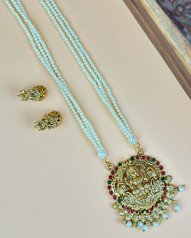 Gold necklace with blue beads and a decorative pendant on a beige surface.