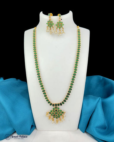 Green beaded necklace and earrings on a white stand with blue fabric background