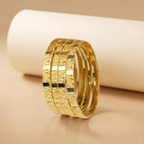 A stack of three gold-plated rings with a textured circular pattern, displayed on a beige surface with a white cylindrical prop in the background.