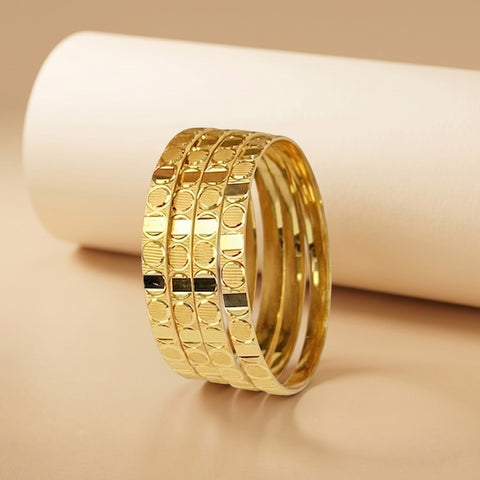 A stack of three gold-plated rings with a textured circular pattern, displayed on a beige surface with a white cylindrical prop in the background.