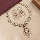 Gold-toned traditional necklace and matching earrings with green enamel, white pearl-like stones, and a small red accent, arranged on a beige surface with decorative box corners.