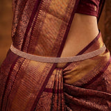 A close-up of a model wearing a traditional Indian saree in deep maroon and gold zari brocade, accessorized with a sparkling rose gold-plated triple-row waist chain.