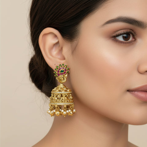 Gold earrings with green and red stones worn by a model on a beige background