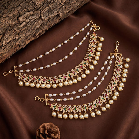 Gold-toned traditional Indian bridal jewelry set featuring a waist chain and matching earrings adorned with white pearls, pink enamel, and green stone accents, displayed on a brown satin fabric background.