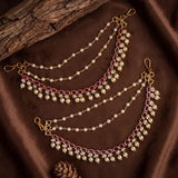 Gold-toned traditional Indian chain waist chains decorated with white faux pearls and purple gemstone accents, arranged on a brown satin fabric background with a piece of wood and a pine cone.
