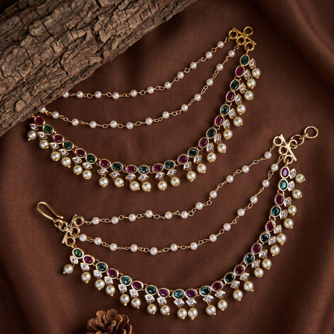 Gold-plated double-layered waist chains decorated with white faux pearls and green and red gemstone clusters, displayed on a brown fabric background with a wood slice prop.