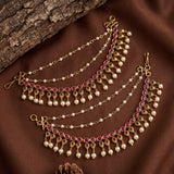 Gold-toned Indian-style chain necklace with pink gemstone accents and white pearl beads, displayed on a brown fabric background with a piece of wood.