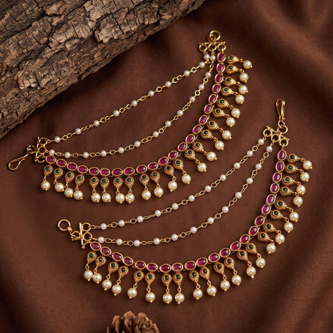 Gold-toned Indian-style chain necklace with pink gemstone accents and white pearl beads, displayed on a brown fabric background with a piece of wood.