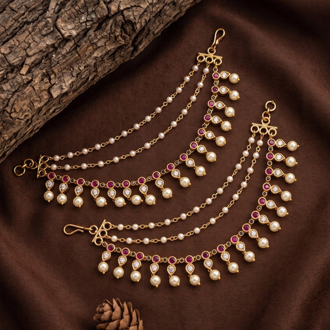 Gold-toned chain waist chains decorated with white faux pearls and pink gemstone accents, arranged on a brown fabric background with a tree branch and pinecone prop.