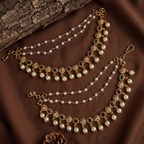 Gold-plated Indian style choker necklace with white faux pearls, green and red stones, and floral motifs, displayed on a brown fabric background.
