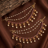 Three gold-toned traditional Indian waist chains decorated with white pearls, red gemstones, and filigree details, arranged on a brown satin fabric with a rustic wood log.