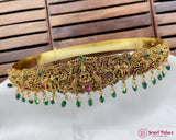 Gold necklace with green and red stones on a white surface with wooden background