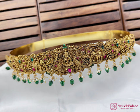 Gold necklace with green and red stones on a white surface with wooden background