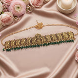 An ornate gold-toned traditional necklace with elephant motifs and a row of dark green bead drops, arranged on pink satin fabric with roses and a candle in the background.