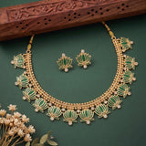 Gold and green lotus necklace set with matching earrings, displayed on a dark green background with a carved wooden prop and small dried flowers.