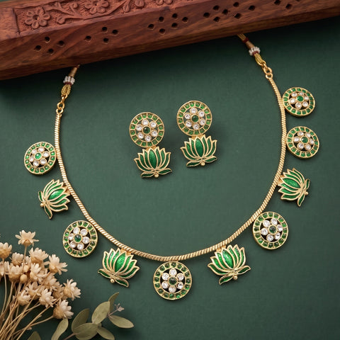 Gold and green lotus jewelry set featuring a necklace, matching earrings, and decorative pendant charms, arranged on a dark green background with dried flowers and a carved wooden prop.
