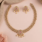 Gold-plated traditional Indian jewelry set featuring a necklace and matching earrings, embellished with small white pearls, clear rhinestones, and pink oval center stones, displayed on a soft pink background.
