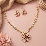 Gold-toned traditional jewelry set featuring a necklace and matching earrings with oval purple stones and clear rhinestone accents, arranged on a soft pink background with decorative burlap and a flower.
