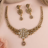Gold-toned traditional necklace and matching drop earrings set with intricate crystal embellishments, displayed on a soft pink background.