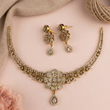 Gold-toned jewelry set with a necklace and matching earrings, decorated with clear rhinestones and featuring teardrop-shaped crystal drops, arranged on a soft pink background with neutral fabric and twine props.